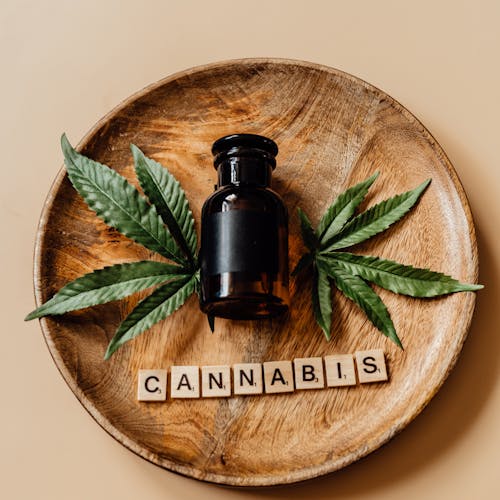 A bottle of cannabis surrounded by leaves on a wooden plate with scrabble tiles.